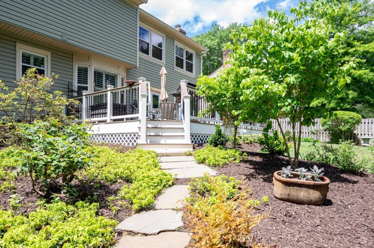Backyard Trex composite deck renovation in Alexandria, VA surrounded by mature trees, garden beds, and a stone walkway leading to the deck.