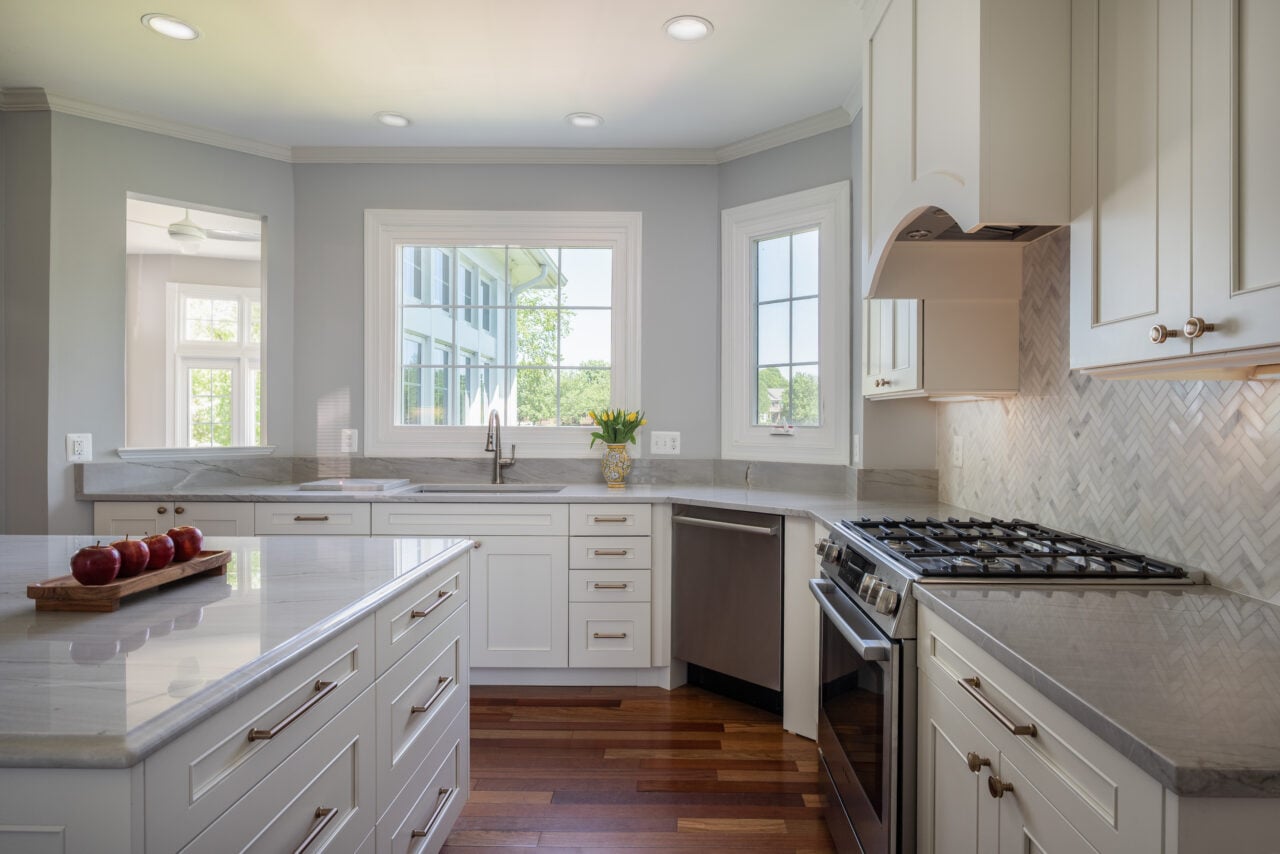 Bright Leesburg, VA kitchen renovation with quartz island, white shaker cabinets, stainless steel dishwasher and gas range, and oversized windows.