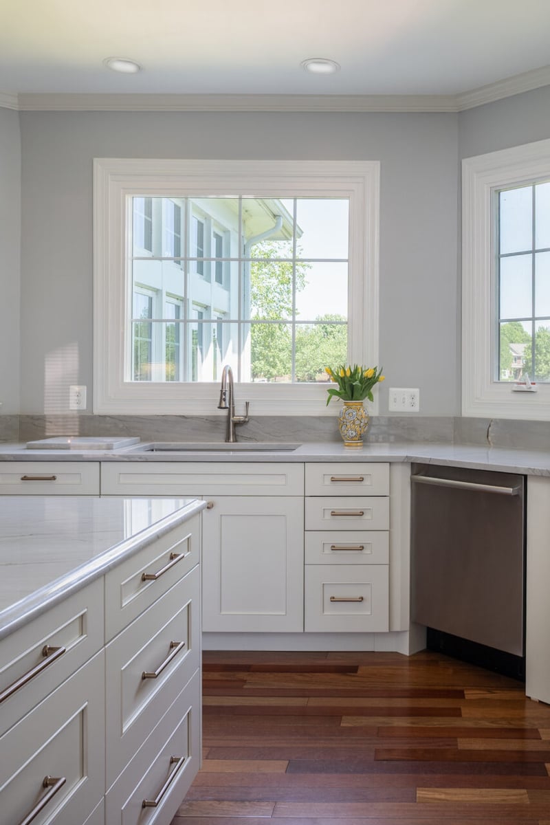 Custom kitchen remodel in Leesburg, VA featuring a quartz-topped island, stainless steel sink and dishwasher, white shaker cabinetry, and dark hardwood flooring.