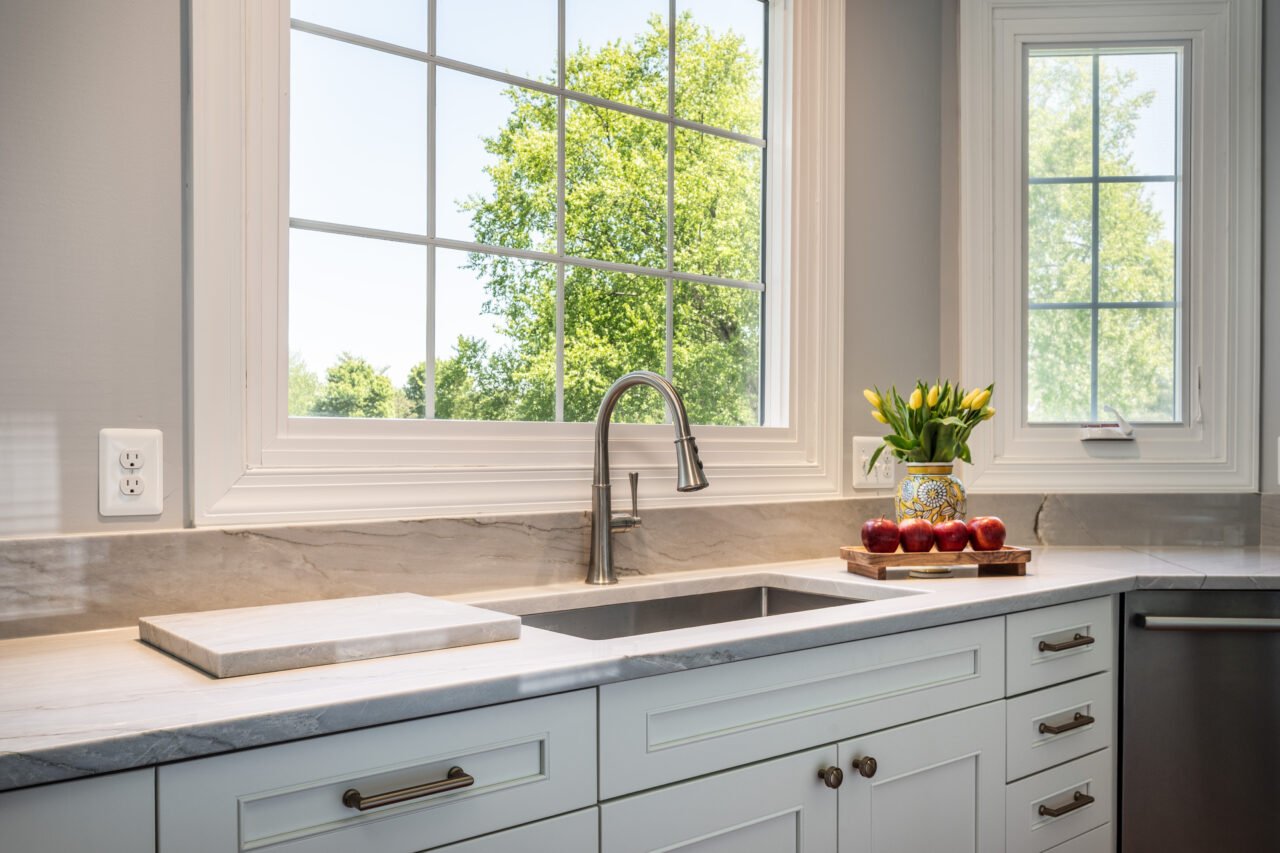 Remodeled kitchen sink area in Leesburg, VA with stainless steel farmhouse sink, quartz countertops, and natural light from multiple windows.