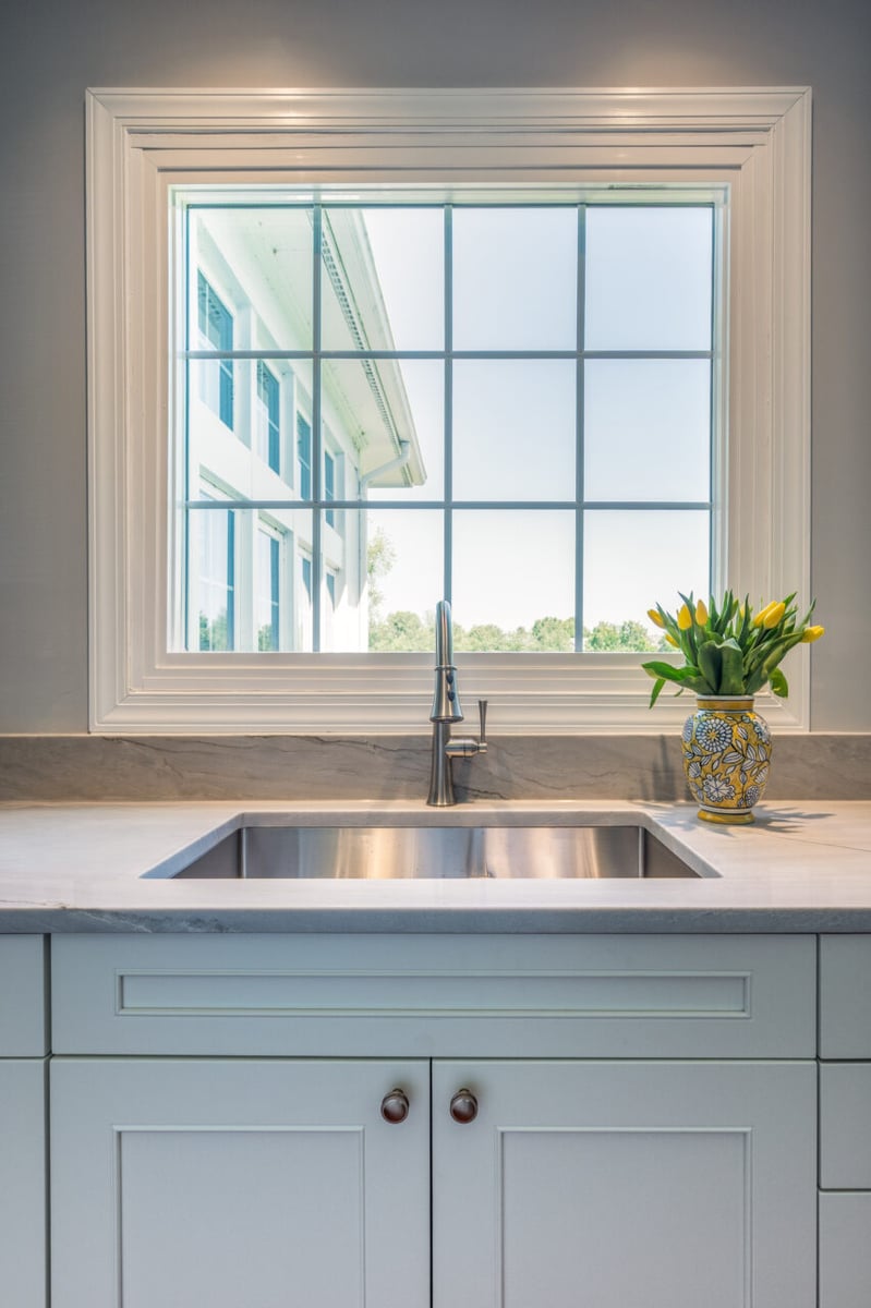 Kitchen sink view beneath a large window in a Leesburg, VA kitchen remodel with white cabinetry and quartz surfaces.