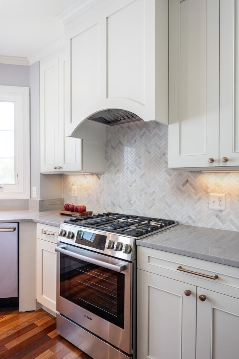 Stainless steel gas range with custom vent hood and herringbone tile backsplash in a luxury Leesburg, VA kitchen renovation