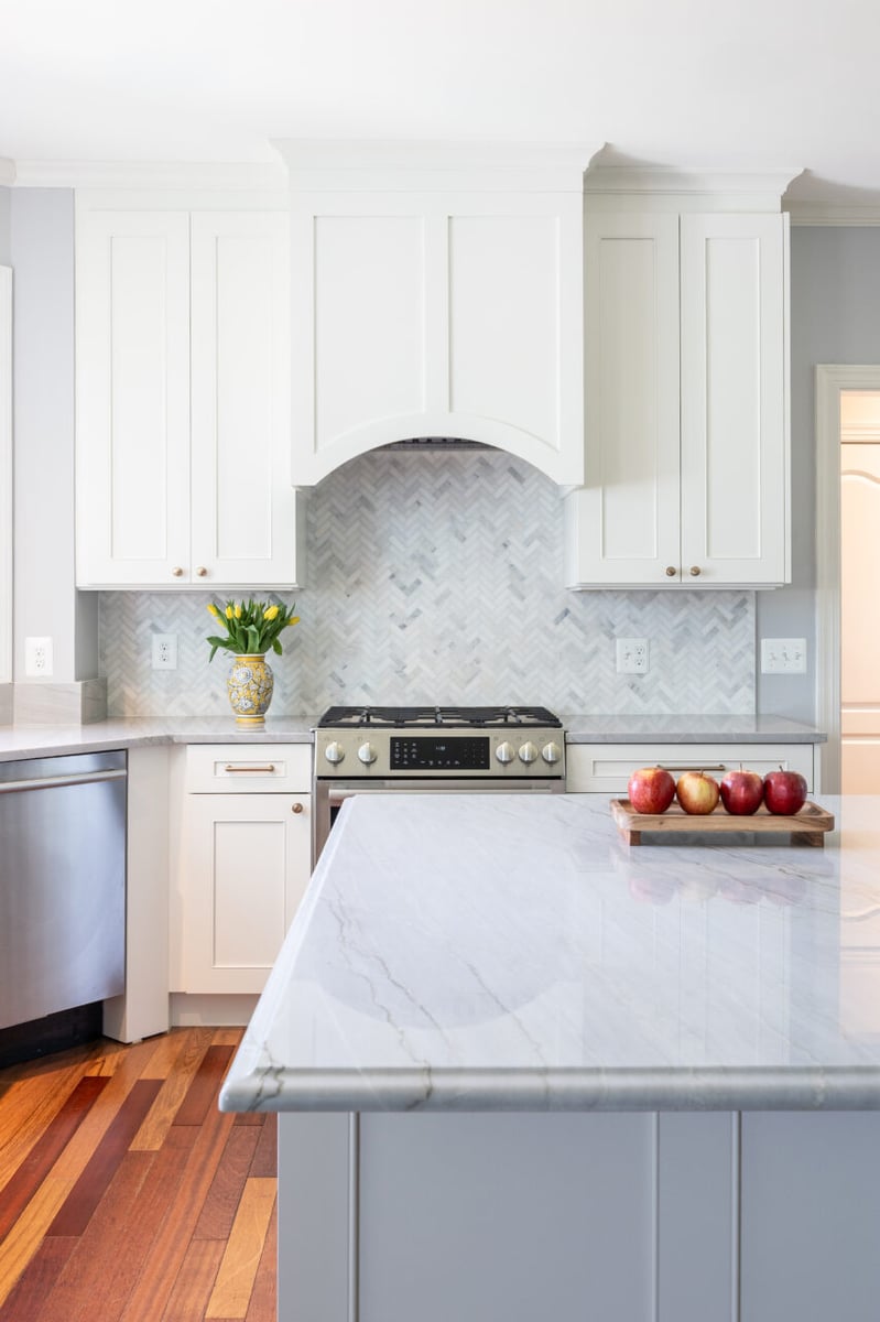Large quartz waterfall-style island overlooking custom cabinetry, gas range, and herringbone tile backsplash in a remodeled Leesburg, VA kitchen.