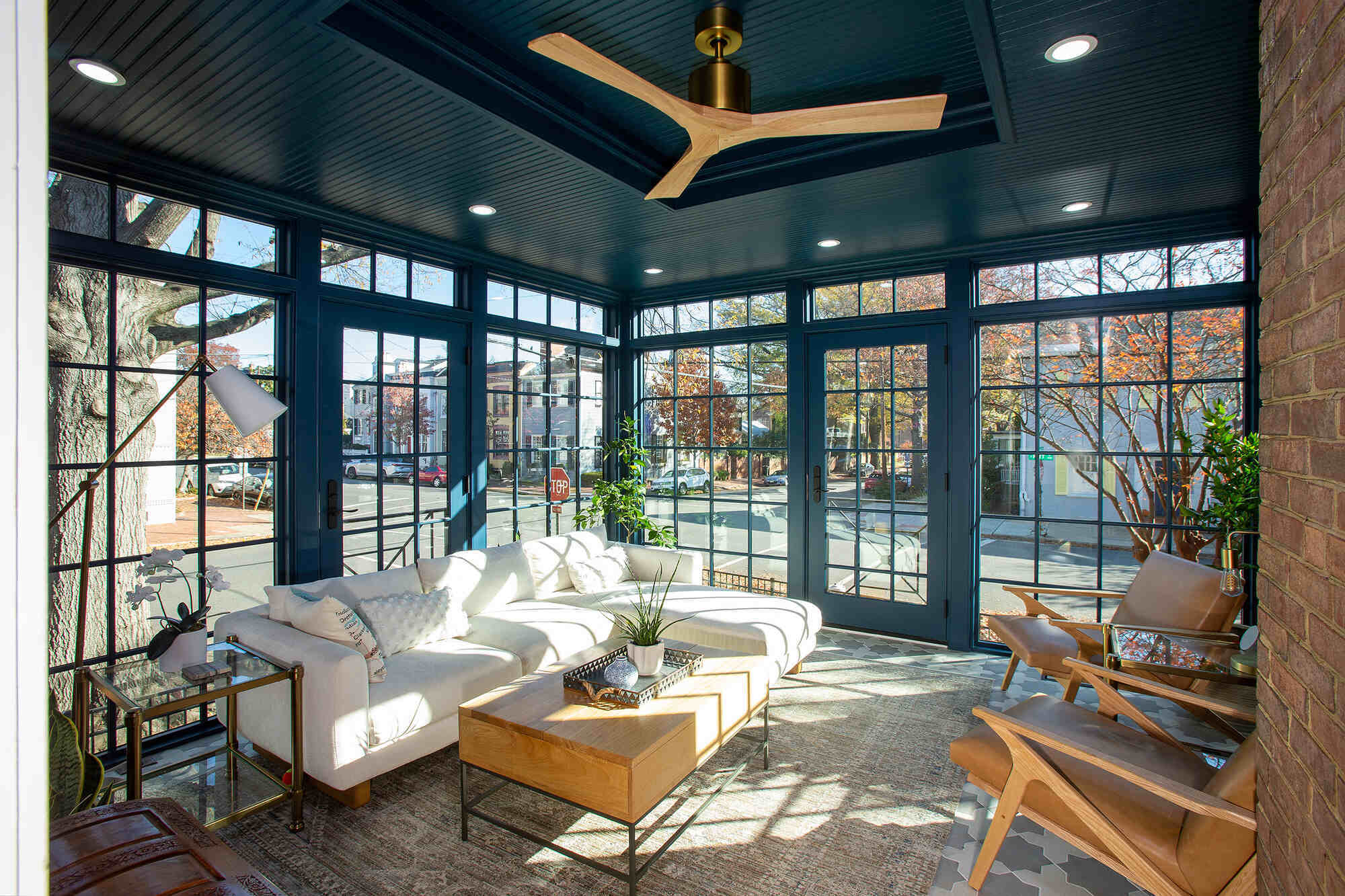 Glass-paneled sunroom with white sectional and natural light by Anchor Remodel in Alexandria, VA