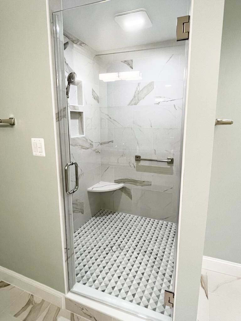 Frameless glass walk-in shower with marble tile and bench by Anchor Remodel in McLean, VA.