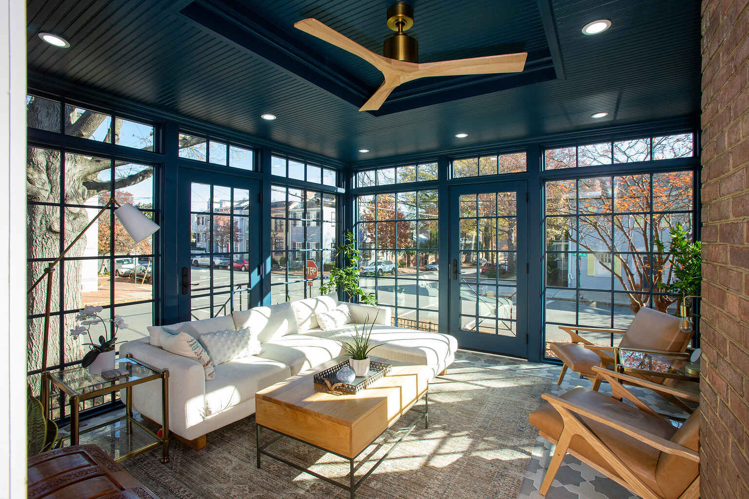 Glass-paneled sunroom with white sectional and natural light by Anchor Remodel in Alexandria, VA