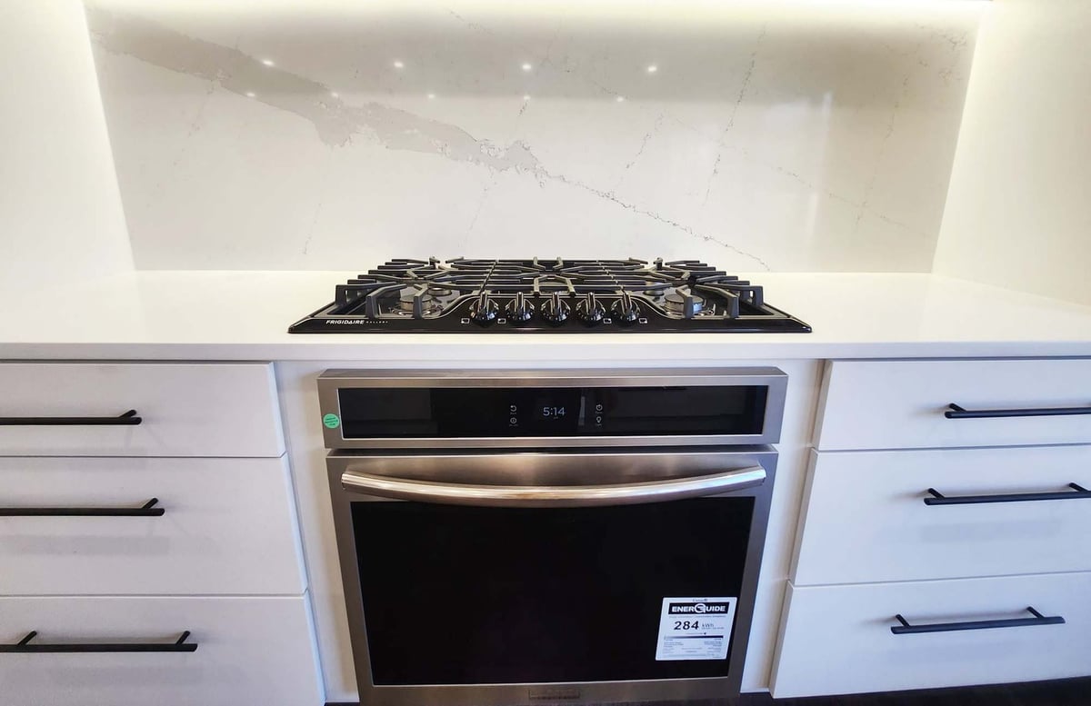 Modern gas range with wood cabinetry and quartz backsplash by Anchor Remodel in Alexandria, VA.