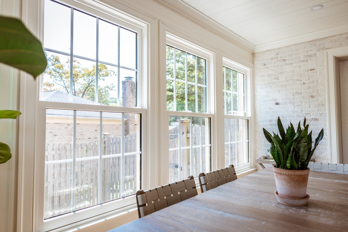 Sunroom dining area with potted snake plant and brick accent wall by Anchor Remodel in Alexandria, VA