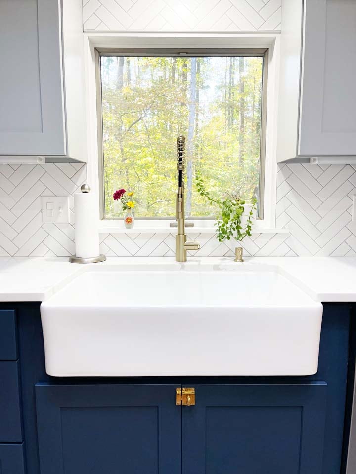 Centered farmhouse sink in kitchen with herringbone tile and gold faucet by Anchor Remodel in Springfield, VA.