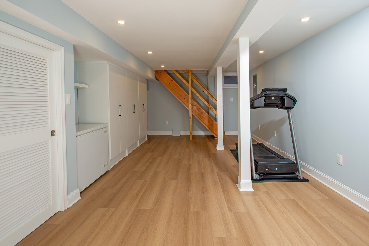 Custom basement update with wood staircase and treadmill by Anchor Remodel in Springfield, VA.