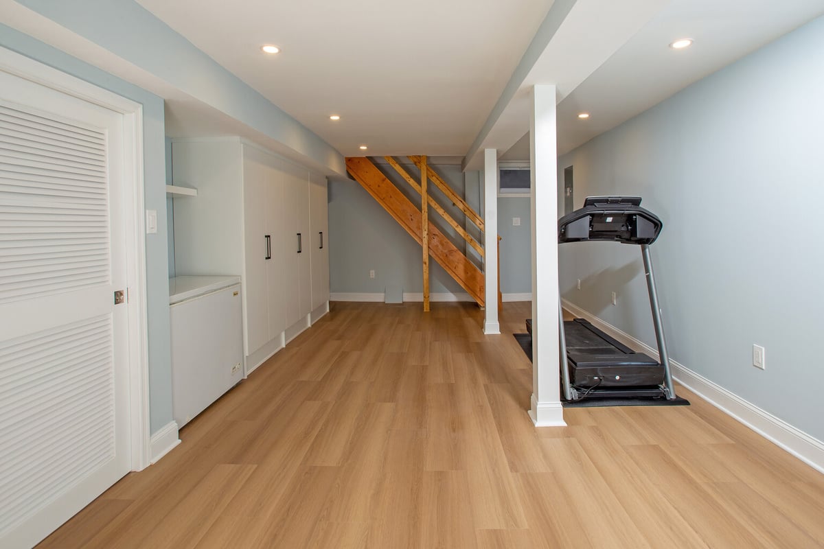 Custom basement update with wood staircase and treadmill by Anchor Remodel in Springfield, VA.