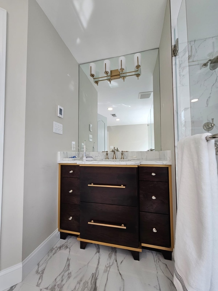 Custom wood vanity with marble counter and gold hardware in Leesburg bath remodel by Anchor Remodel.