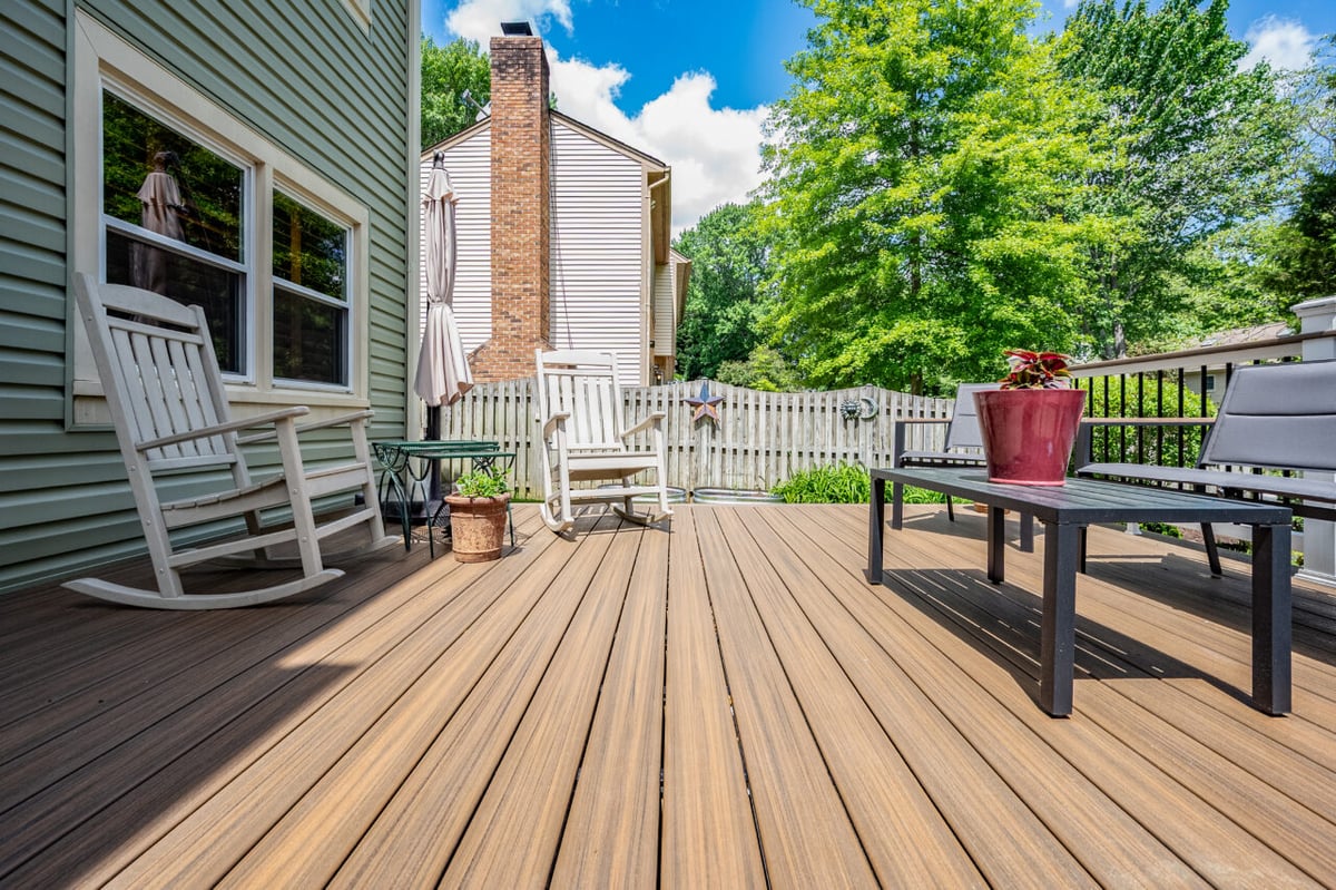 Deck remodel in Alexandria, VA featuring Trex composite decking, outdoor lounge seating, rocking chairs, and modern railing overlooking a landscaped backyard.