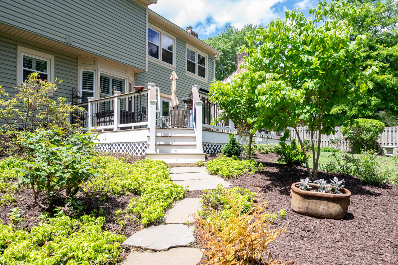 Backyard Trex composite deck renovation in Alexandria, VA surrounded by mature trees, garden beds, and a stone walkway leading to the deck.