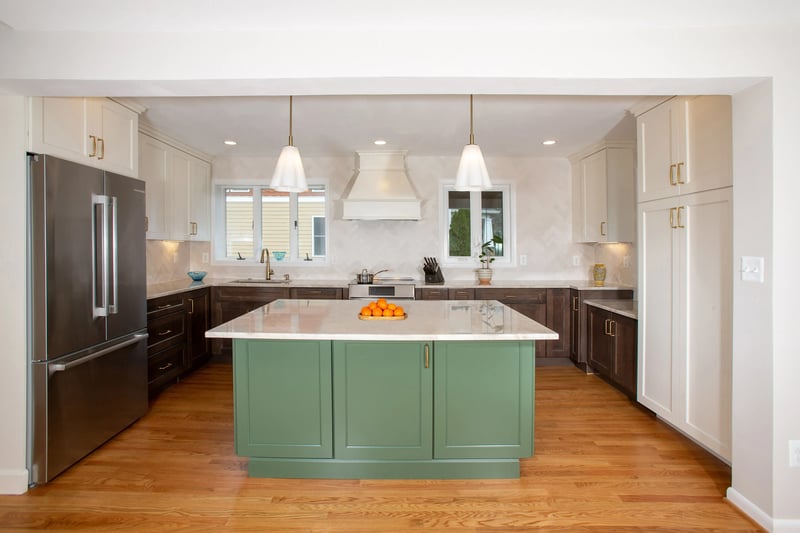 Bright, modern kitchen view with a large center island with green cabinets under off-white countertops, dark wood cabinets along the back wall, a stainless steel fridge, and pendant lighting over the island