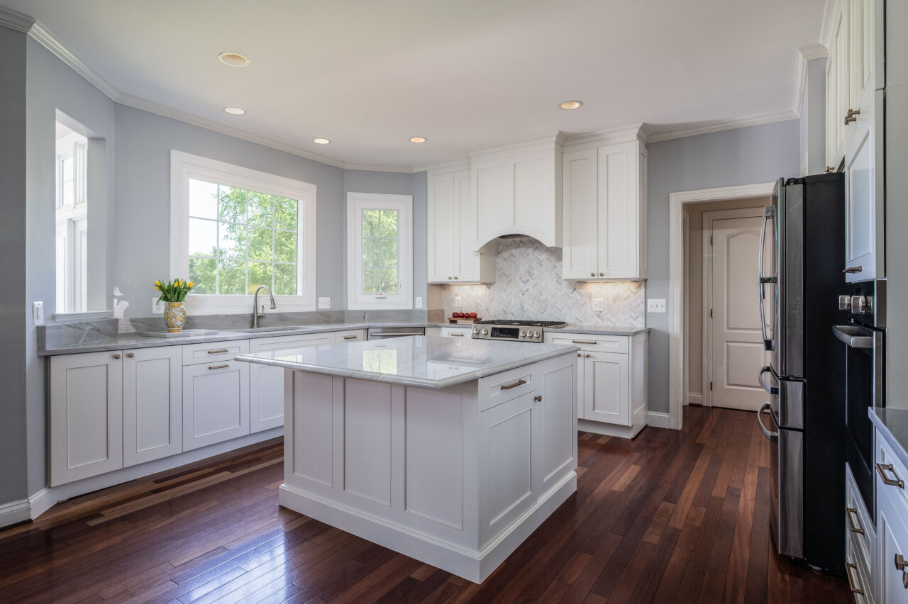Bright kitchen remodel in Leesburg, VA featuring white shaker cabinets, a large quartz island, marble-look countertops, gray walls, and dark hardwood flooring.
