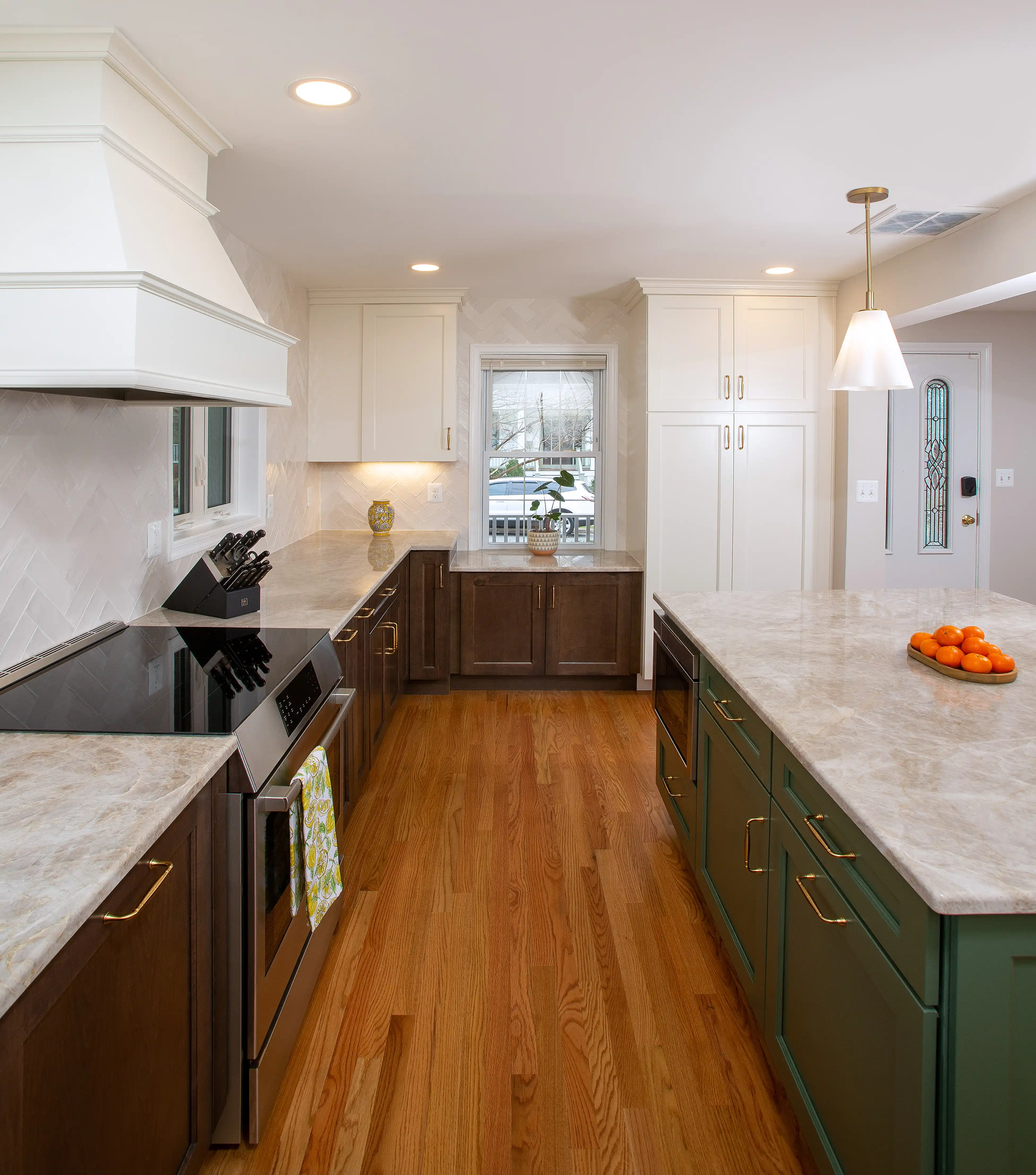 Kitchen view featuring a custom white range hood, large island with green cabinetry, and white and brown wall cabinets with brass hardware