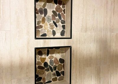 Two recessed shower niches with pebble stone tile backing and black trim set into beige tiled walls