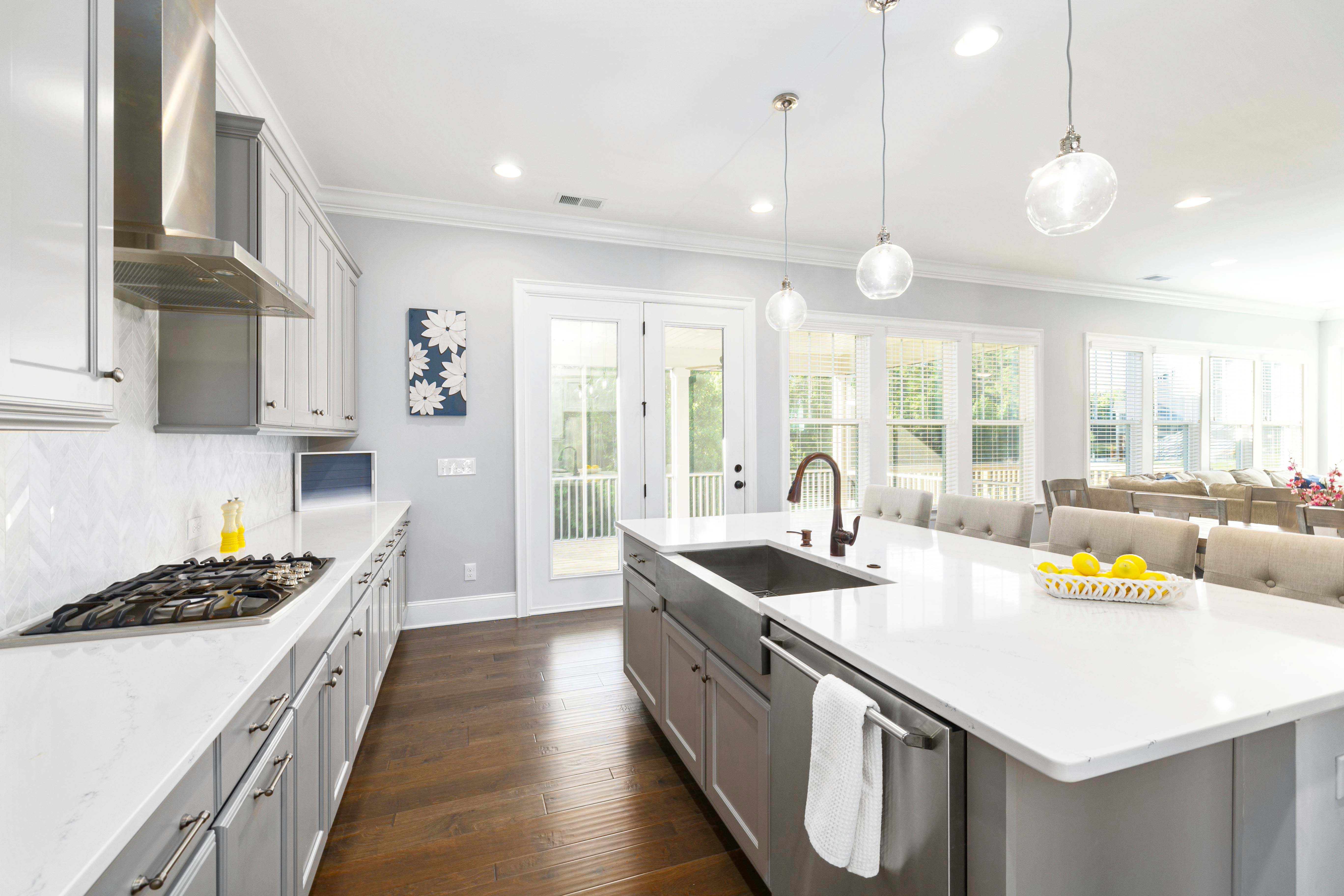 Bright and modern kitchen featuring sleek white countertops, gray cabinets, a spacious island with farmhouse sink, stainless steel appliances, and ample natural light for a welcoming, functional space.